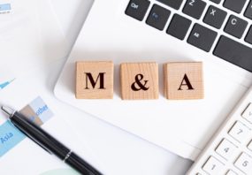 Wooden blocks with the characters 'M&A' spelled out on top of an open laptop